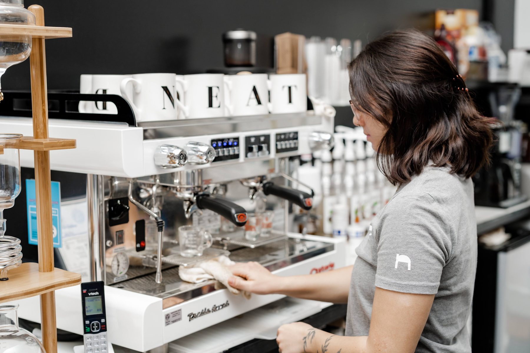A barista cleaning the espresso machine with NEAT mugs on top