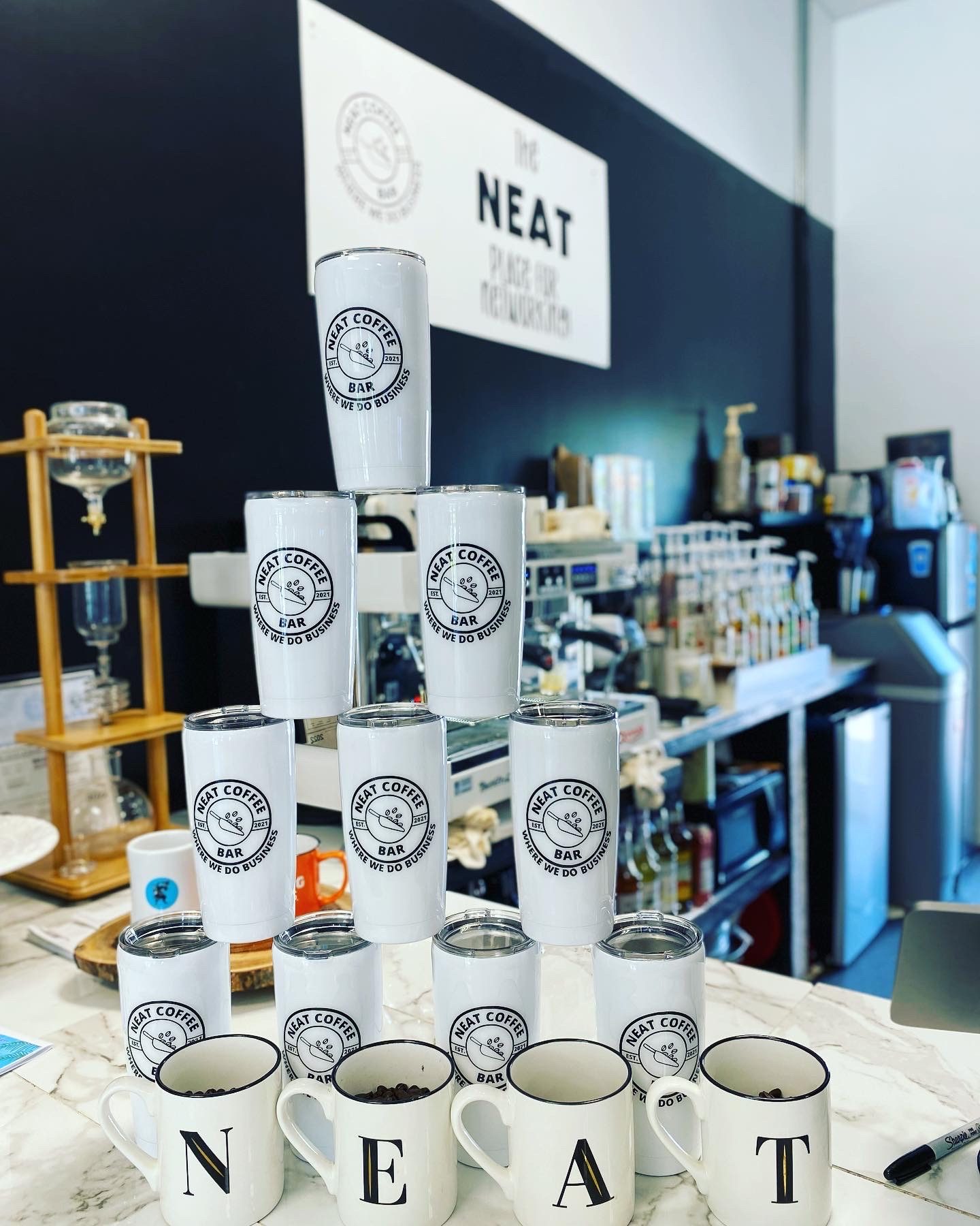 A pyramid of NEAT branded tumblers and mugs spelling NEAT on the counter