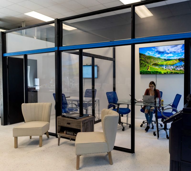 Glass-walled co-working room with a member working on a laptop at NEAT Coffee Bar